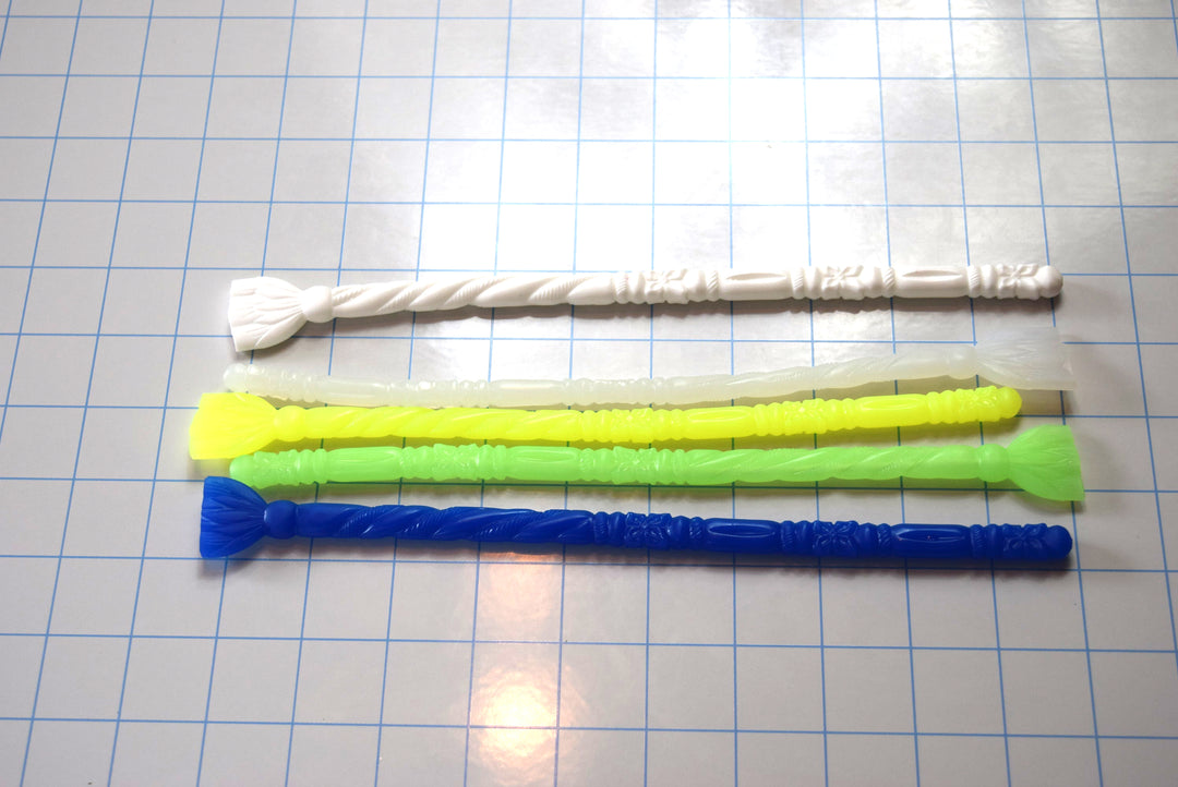 Lineup of four SSND-FLORENTINE10 silicone sounds in translucent white, translucent yellow, translucent green, and translucent blue, each featuring elliptical tips, florettes, barrel sections, ribs, twisted rope textures, retaining balls, and safety flanges on a blue grid background.
