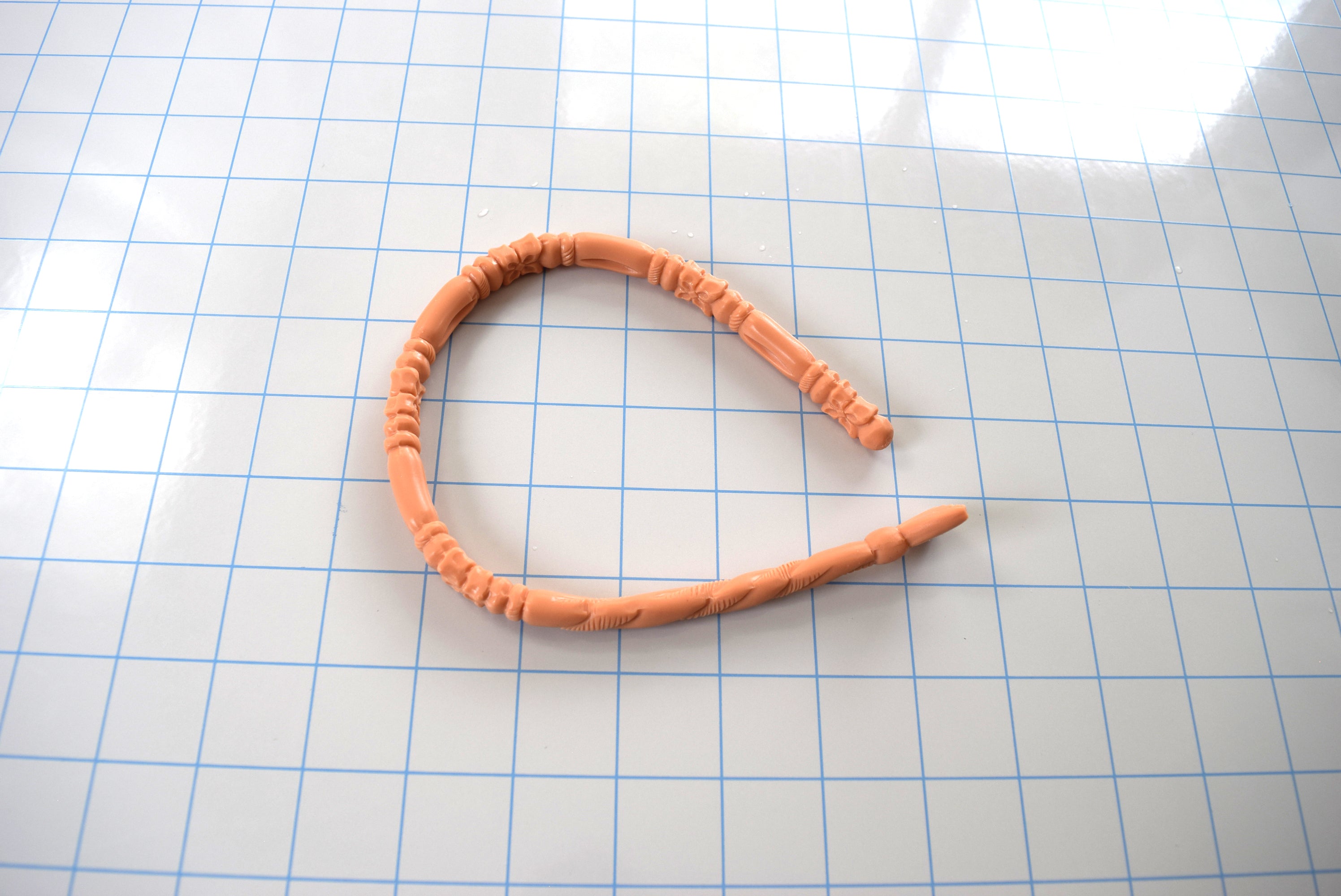 Peach-colored SSND-FLORENTINE14 textured silicone sound curved into a horseshoe shape on a blue grid mat, highlighting its flexibility.