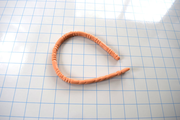 Peach-colored SSND-FLORENTINE14 textured silicone sound curved into a horseshoe shape on a blue grid mat, highlighting its flexibility.
