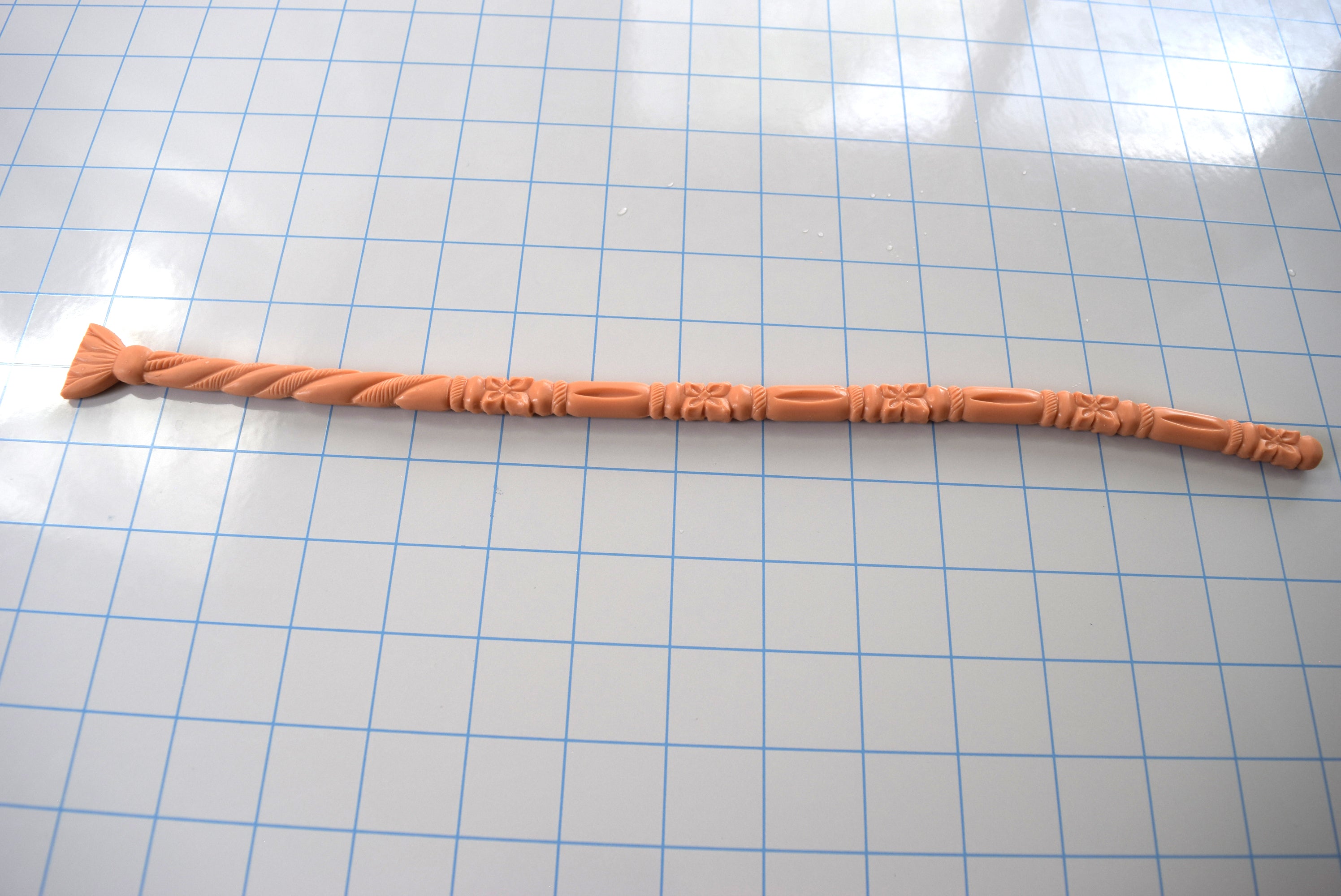 Peach-colored SSND-FLORENTINE14 textured silicone sound with florets, twisted rope patterns, and a flared fan-style safety base laid horizontally on a blue grid mat.