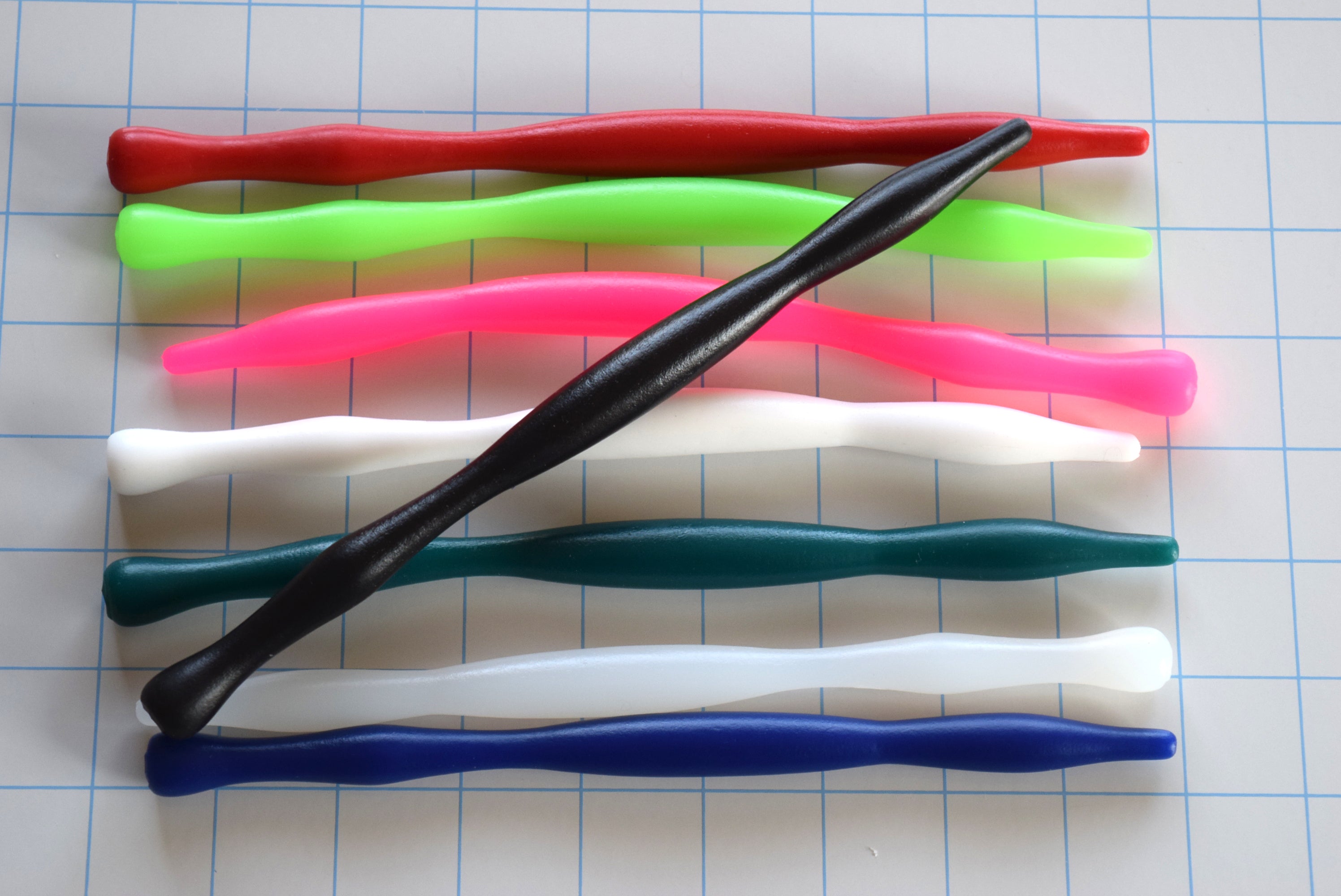 A black silicone sensory barrel sound laid diagonally across a stack of colorful sounds on a grid background.