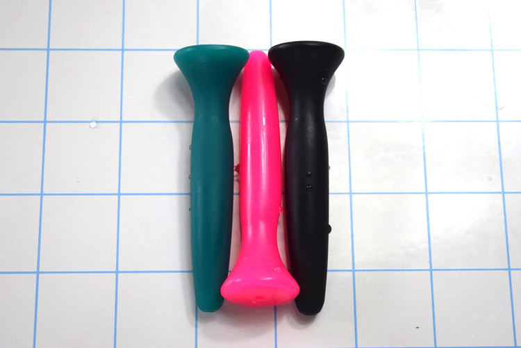 SSND-JWW 6 silicone urethral sound shown vertically in three color choices—teal green, bright pink, and black—on a white surface with a 1"x1" blue grid layout, displaying the 13.5mm peak diameter shaft, 11mm retention valley, and flared safety flange base.