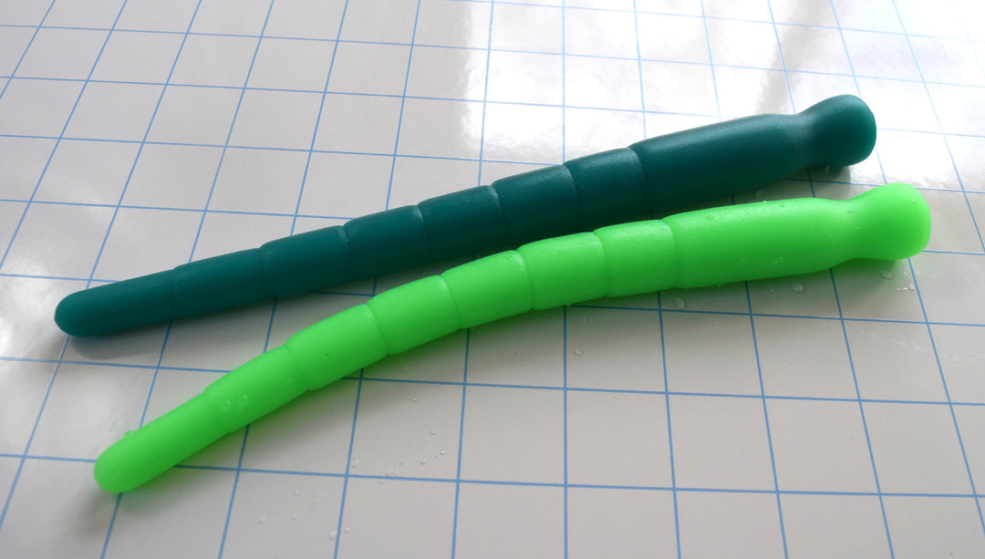 Two multi-dimensional silicone stretching sounds in dark teal and neon green lying side by side on a blue grid surface.