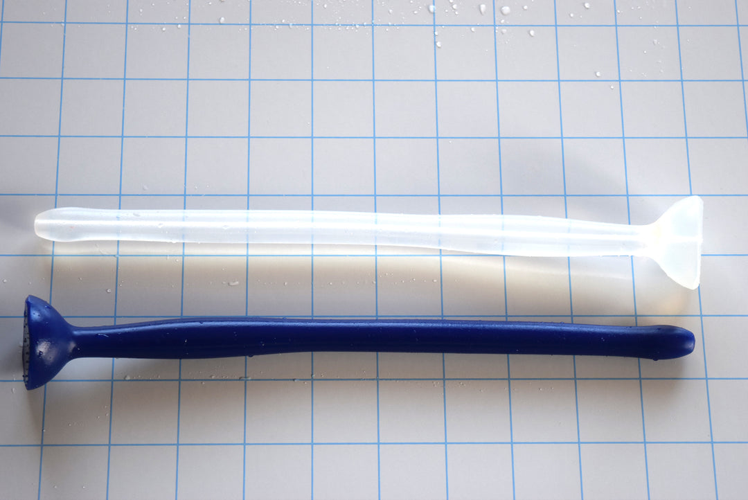 Dark blue and translucent white SSND-MGCWAND10 silicone sounds, 10 inches long, featuring a 13.5mm tip, 15.8mm oval expansion node, 11.5mm retention valley, and extra-large safety flange on a blue grid background.
