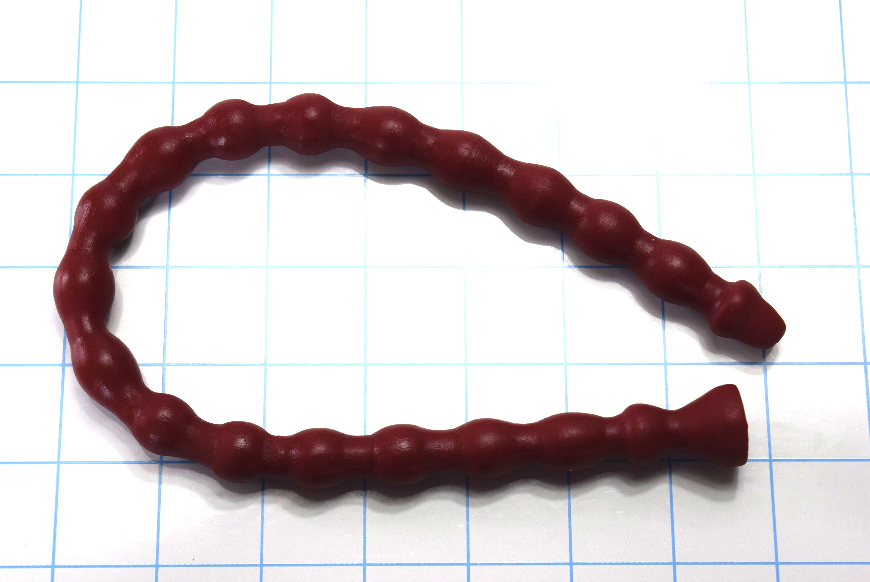 A dark red silicone multi-ribbed sound curves looped across a blue grid background showing distinct nodes and a flared base.