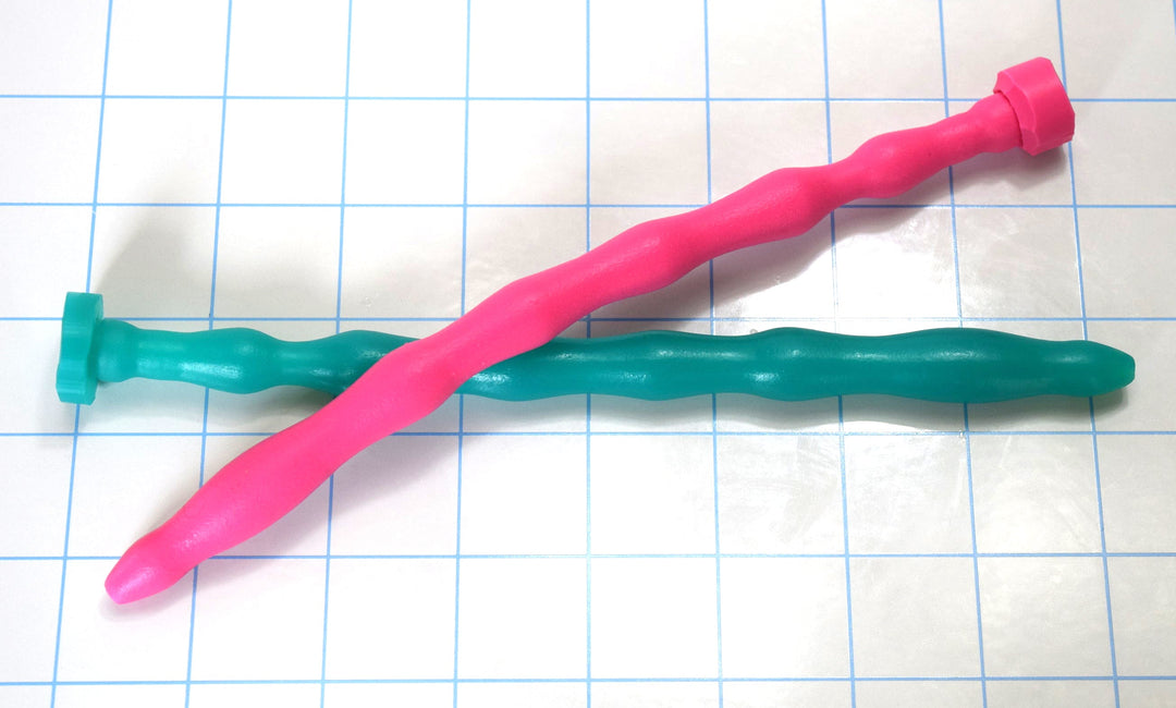 Pink and teal 7-rib multi-dimensional flexible silicone urethral sounds crossed on a blue grid background.