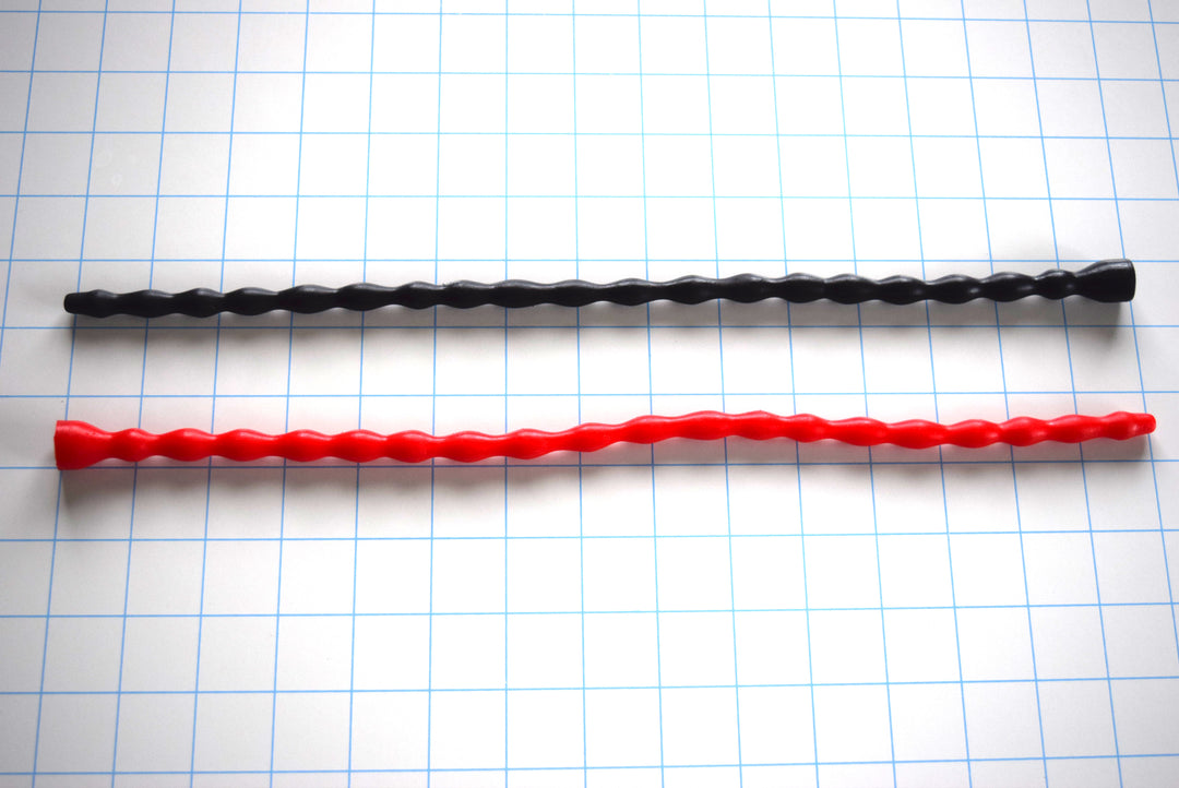 SSND-MRB 6-10 multi-ribbed silicone sounding rods in black and bright red shown laid out horizontally on a white background with 1-inch blue grid lines, featuring 19 elliptical ribs, an 8mm retention valley, and a flared safety base flange.