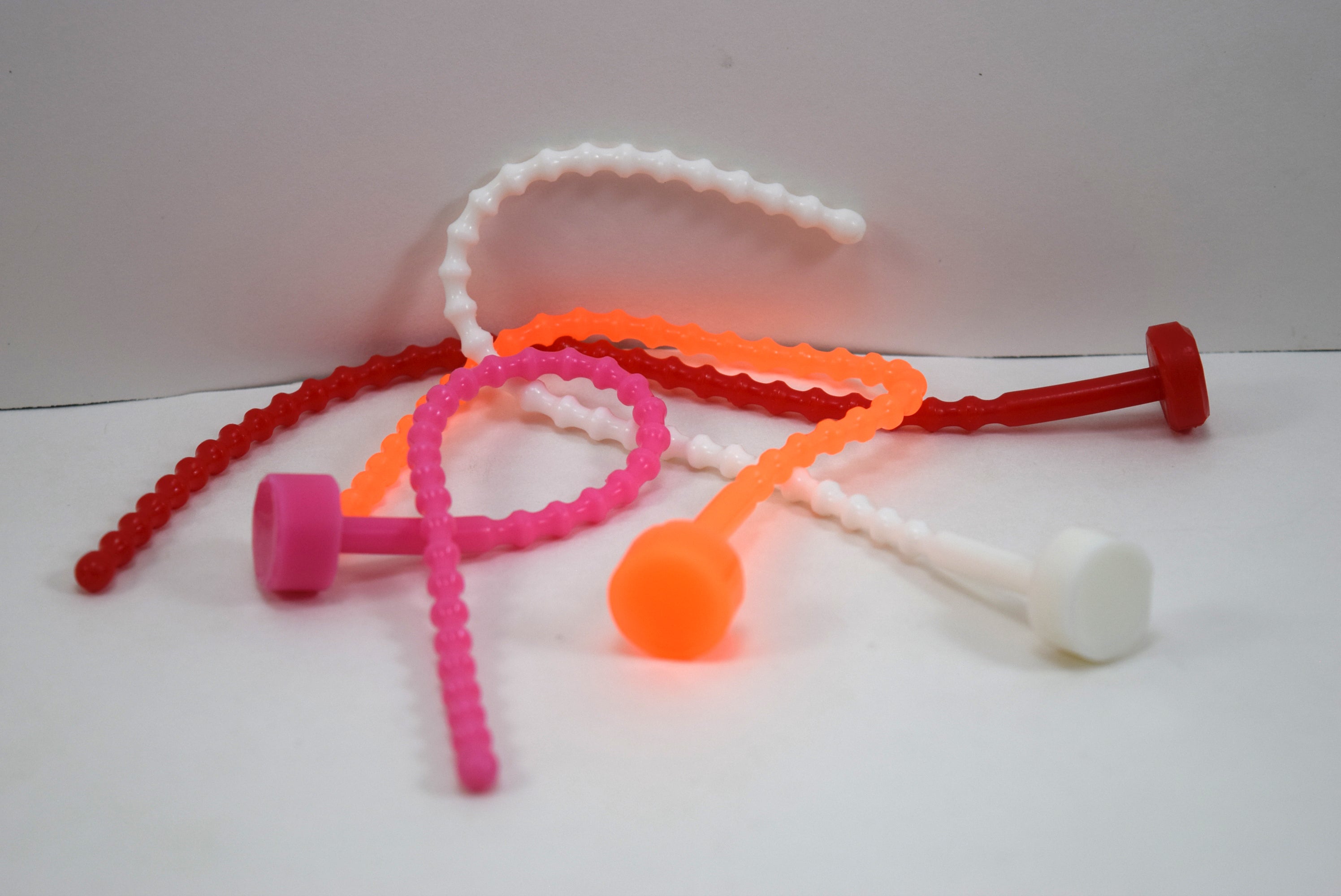 Alternative arrangement of soft, flexible SSND-RIB6 silicone urethral sounds in pink and red displaying 29 ribbed contours along the shaft, 6mm diameter, and flanged safety base.