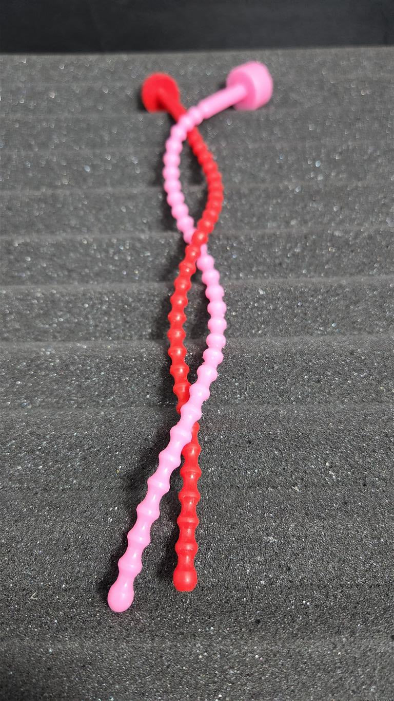 Two soft, flexible SSND-RIB6 silicone urethral sounds in pink and red curled together on a grey background, displaying 29 ribbed contours, 6mm diameter, and flanged safety base.