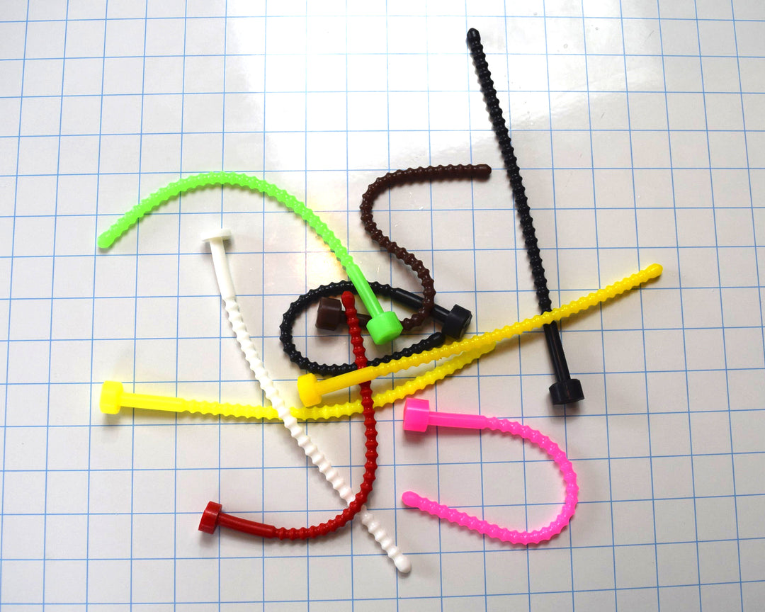 Assortment of soft, flexible SSND-RIB8 silicone urethral sounds in various colors, showing 29 ribbed contours along the shaft, 9-inch insertable length, and flanged base on a blue grid background.