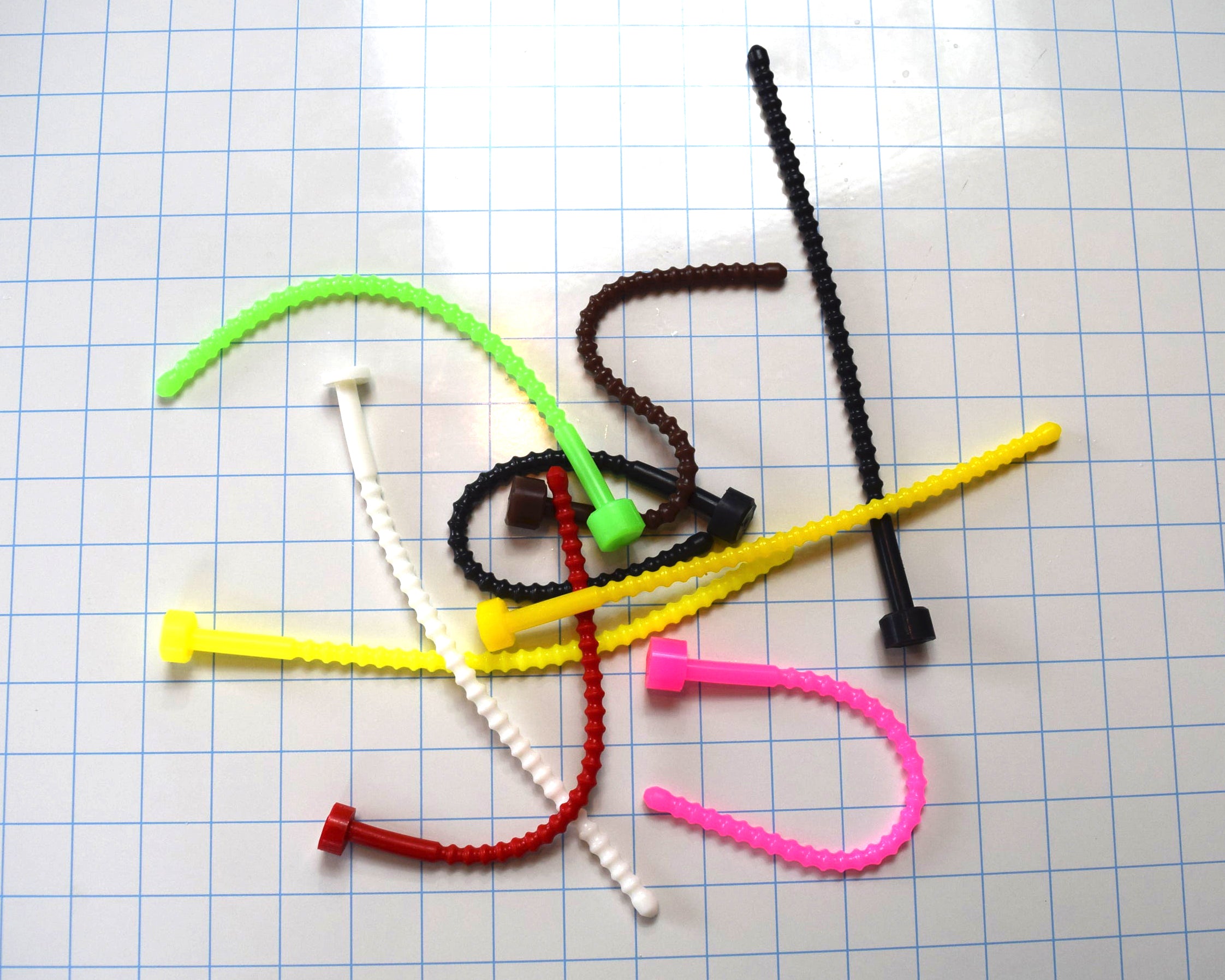 Assortment of soft, flexible SSND-RIB8 silicone urethral sounds in various colors, showing 29 ribbed contours along the shaft, 9-inch insertable length, and flanged base on a blue grid background.