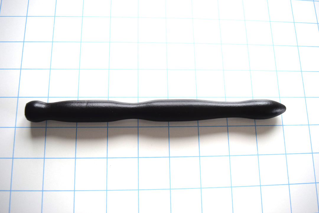 SSND-RIPPLE 6-18 large black silicone urethral sound shown horizontally on a white background with 1"x1" blue grid squares from Screenshot 2026-07-02 154307.jpg, showcasing its three massive expanding wave ripples peaking at 18mm, 8-inch insertable length, and thick safety flared base.