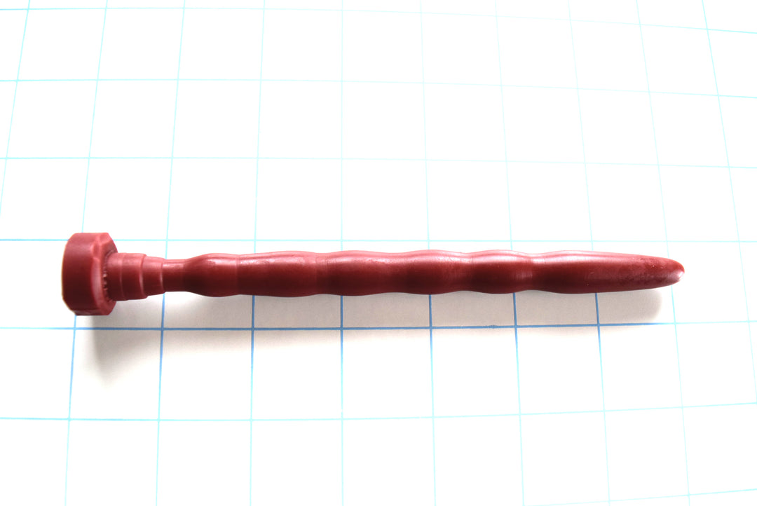 SSND-RIPPLE 8-12 intermediate terracotta-red silicone urethral sound shown horizontally on a white background with 1"x1" blue grid squares from Screenshot 2026-07-02 153626.jpg, showcasing its five undulating wave segments peaking at 12mm, 5.75-inch insertable length, and integrated safety base flange
