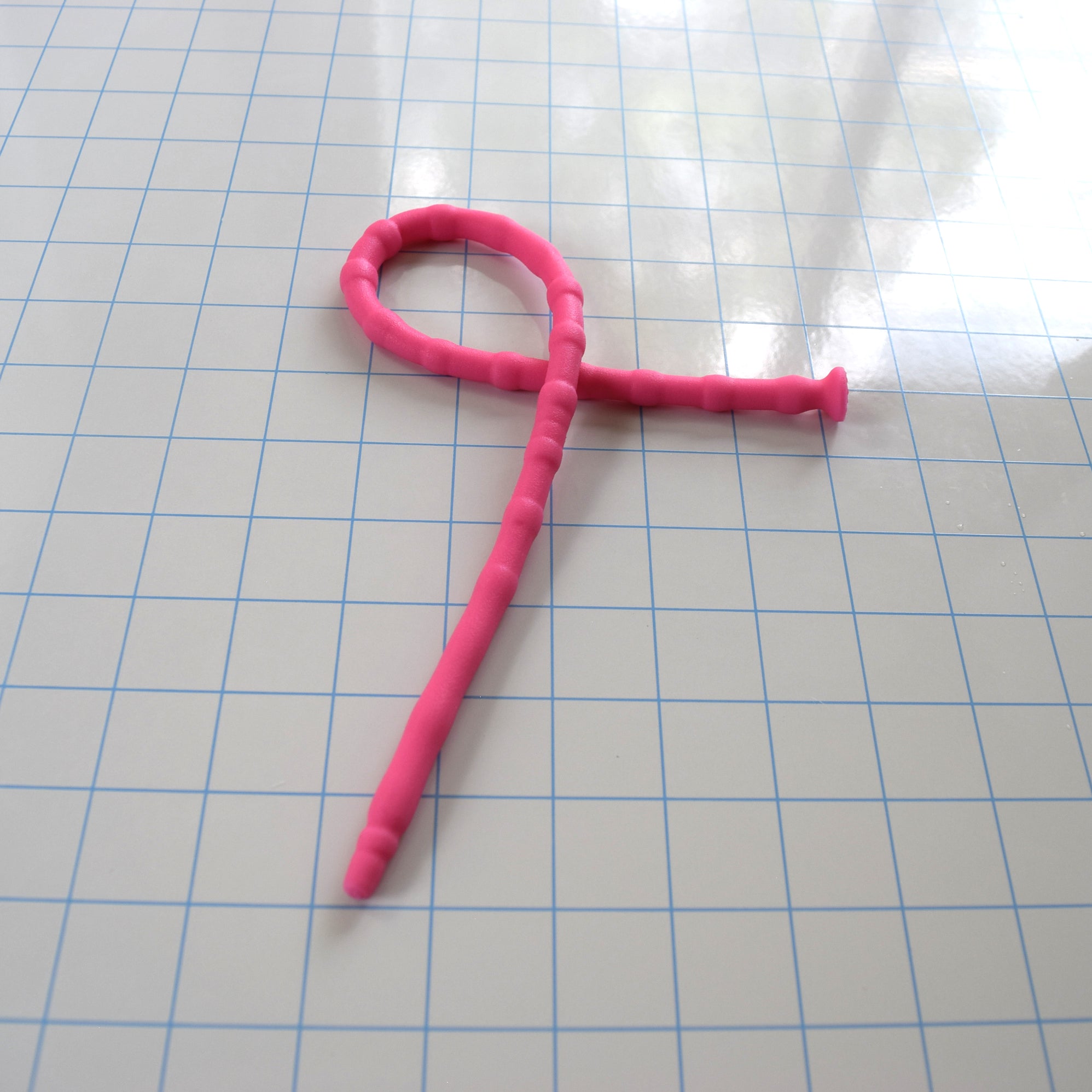 Bright pink SSND-RNDMBALL 7-10mm flexible silicone sound looped onto itself on a blue grid background to demonstrate flexibility.