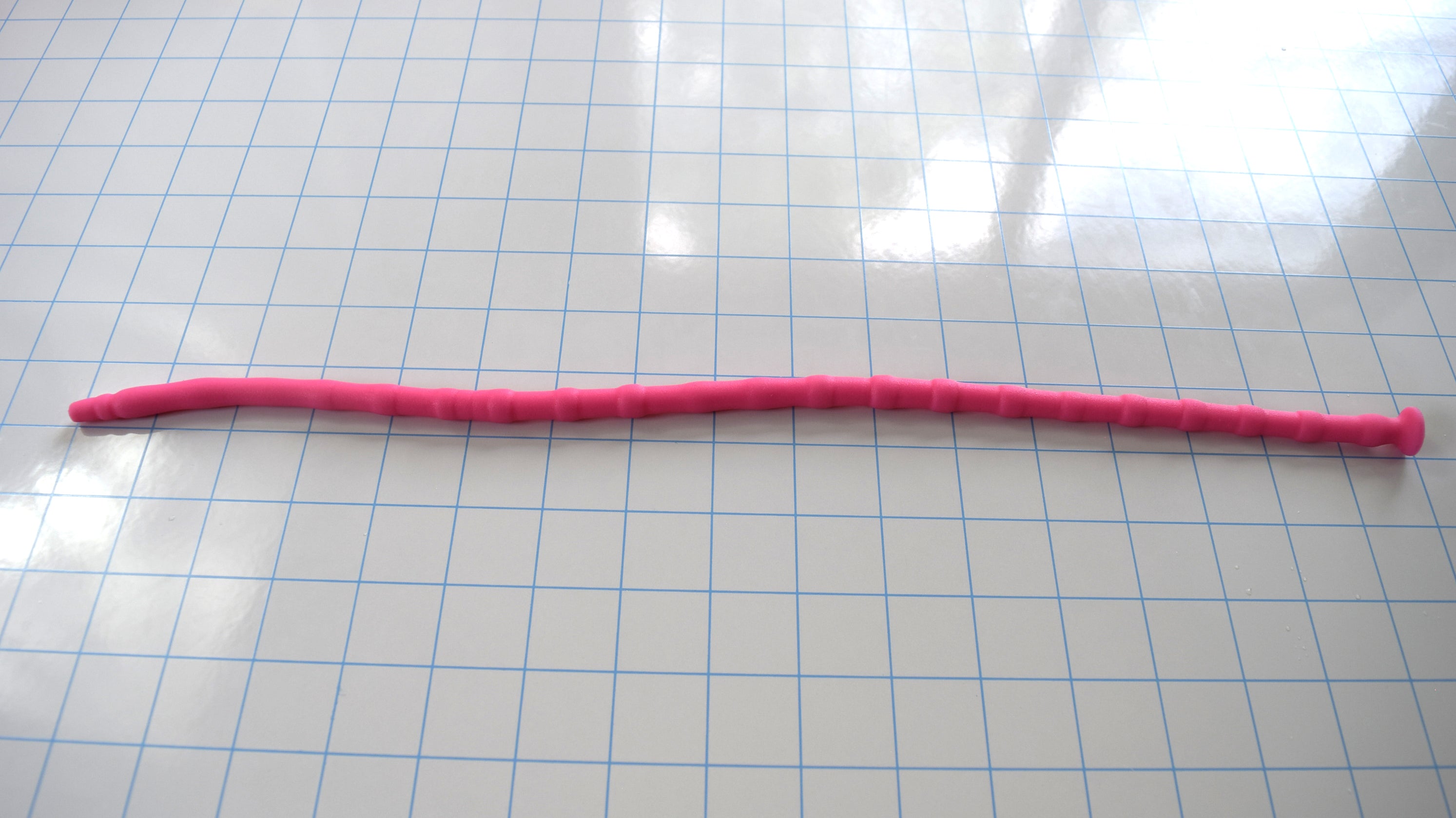 Bright pink SSND-RNDMBALL 7-10mm silicone sound with a multi-ball ribbed shaft and flanged base lying horizontally across a blue grid background.