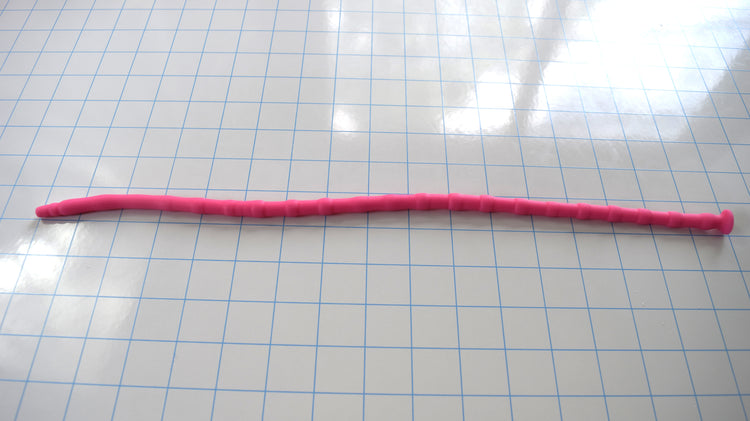 Bright pink SSND-RNDMBALL 7-10mm silicone sound with a multi-ball ribbed shaft and flanged base lying horizontally across a blue grid background.