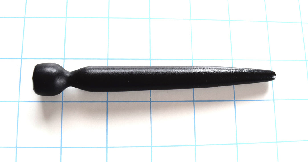 Black tapered silicone urethral sound lying horizontally on a blue grid background.