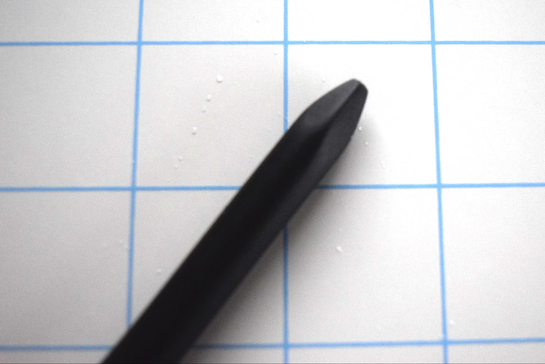 Close-up detail of the blunted spike tip on a black silicone urethral sound against a blue grid background.
