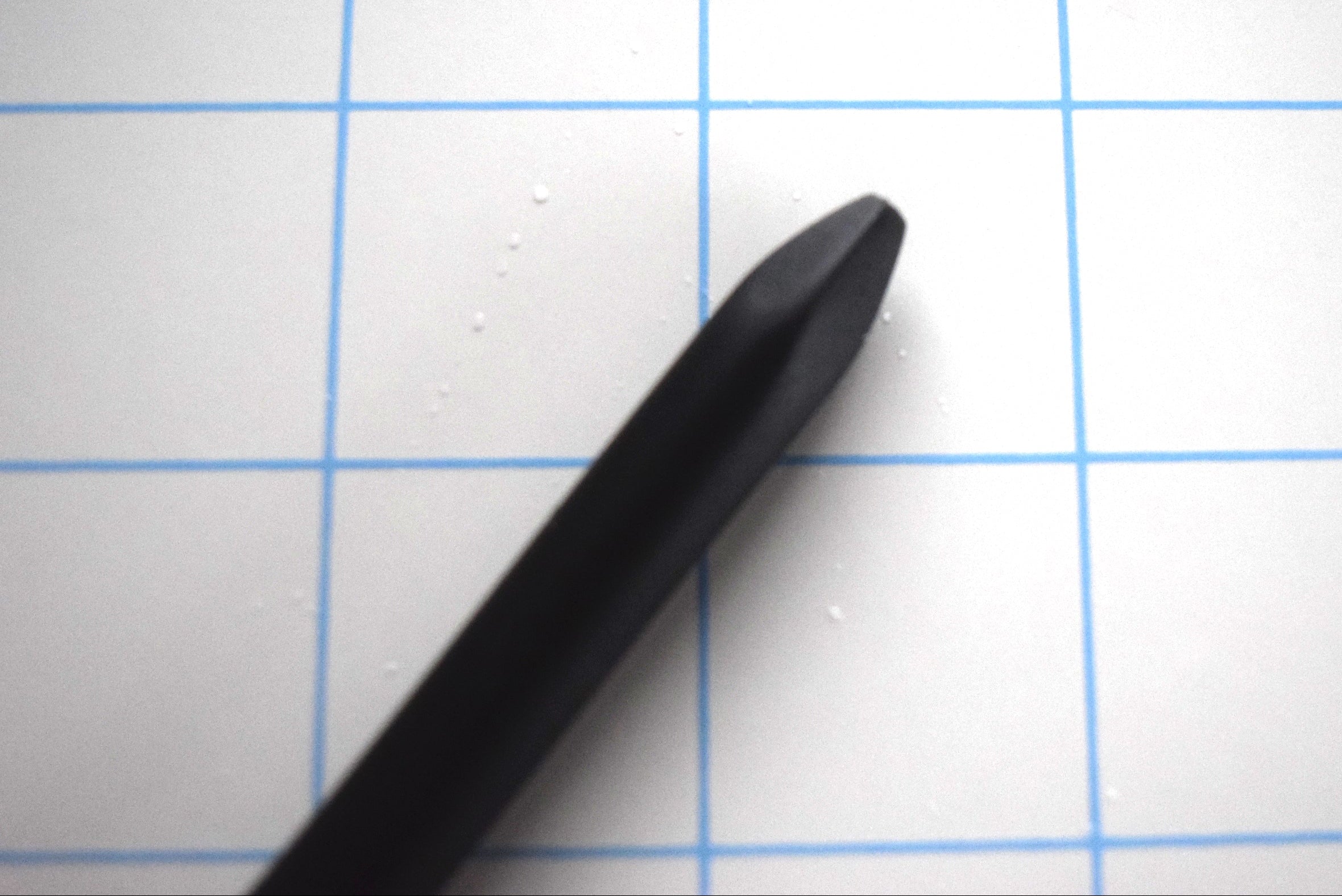 Close-up detail of the blunted spike tip on a black silicone urethral sound against a blue grid background.