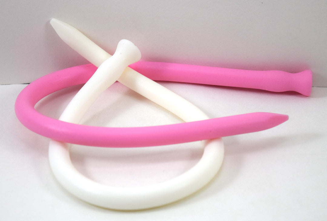 Pink and white flexible spike-tip silicone urethral sounds bent and interlaced together on a white surface.