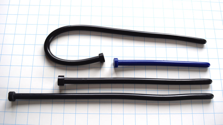 SSND-The Rod 12.5mm smooth silicone urethral sounds shown on a white background with 1"x1" blue grid squares from Screenshot 2026-07-02 134453.jpg, displaying different configurable lengths in black and blue, with one rod flexed into a tight U-shape to demonstrate material flexibility.