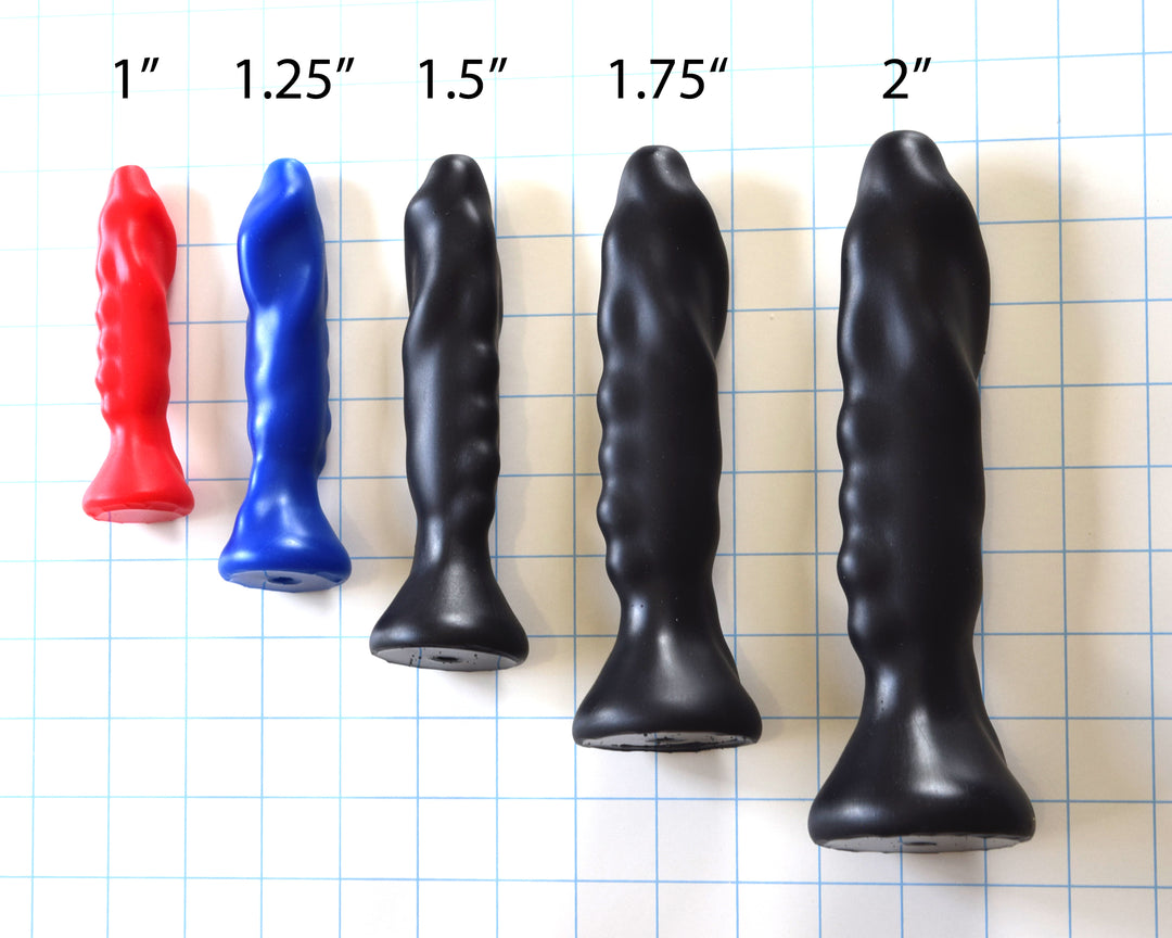 Lineup of SSND-THING silicone enema plugs standing vertically on a blue grid background, labeled by max diameter from 1 inch to 2 inches (1-inch red, 1.25-inch blue, and 1.5-inch, 1.75-inch, and 2-inch in black).