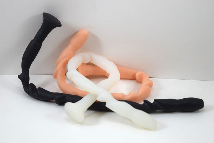SSND-Totem advanced silicone urethral sounds in black, peach, and translucent white variants shown highly flexed and coiled on a plain white background from Screenshot 2026-07-02 133839.jpg, highlighting the unique flattened tapered tip and radical alternating 14mm to 15.5mm ridges.