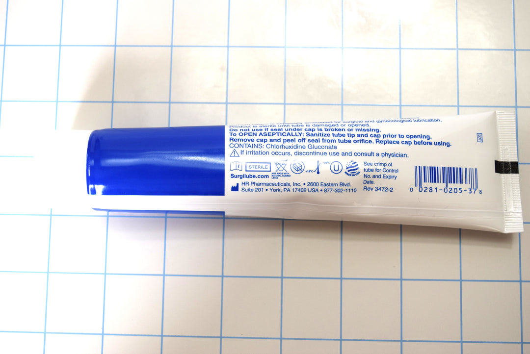 Horizontal back view of Surgilube 4.25 oz flip cap tube showing instructions on a blue grid background.