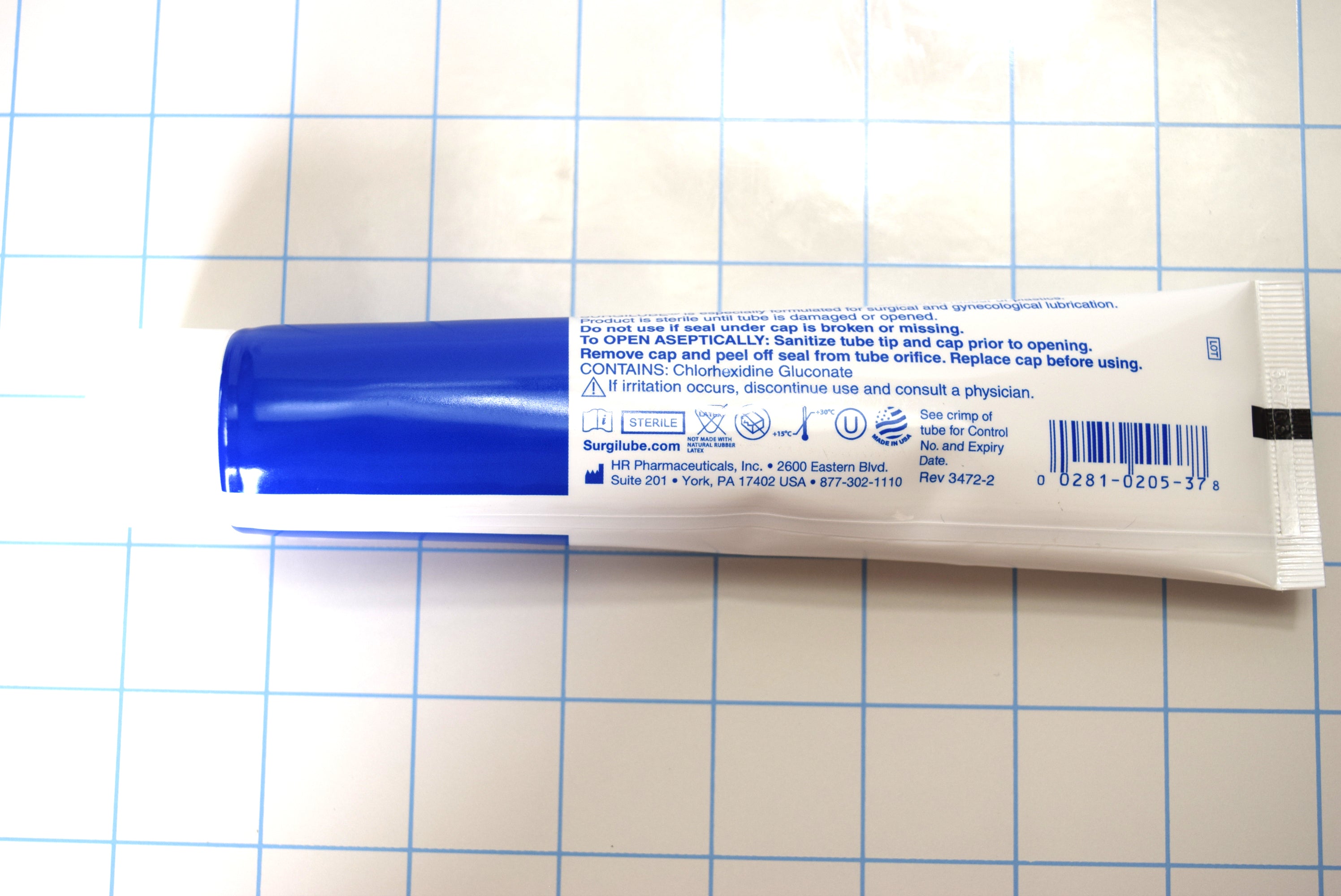 Horizontal back view of Surgilube 4.25 oz flip cap tube showing instructions on a blue grid background.