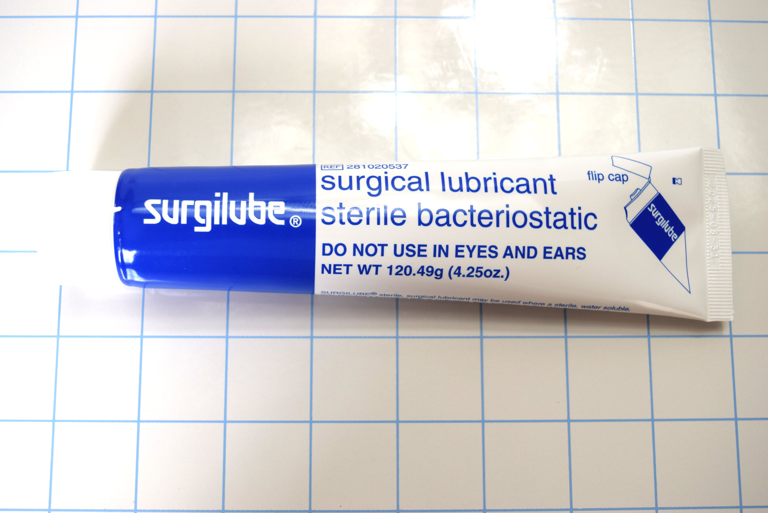 Horizontal front view of Surgilube 4.25 oz flip cap tube on a blue grid background.