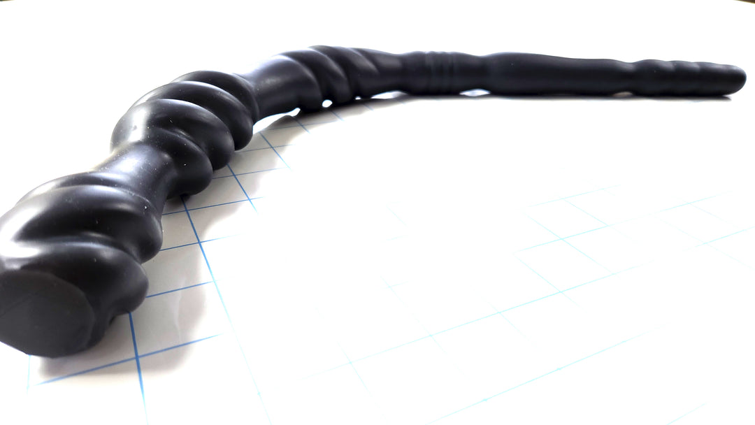 Black Triple Spiral 22-inch silicone nozzle featuring intricate spiraled textures and a graduated design for varied stimulation on a white grid background, showing the flange in focus
