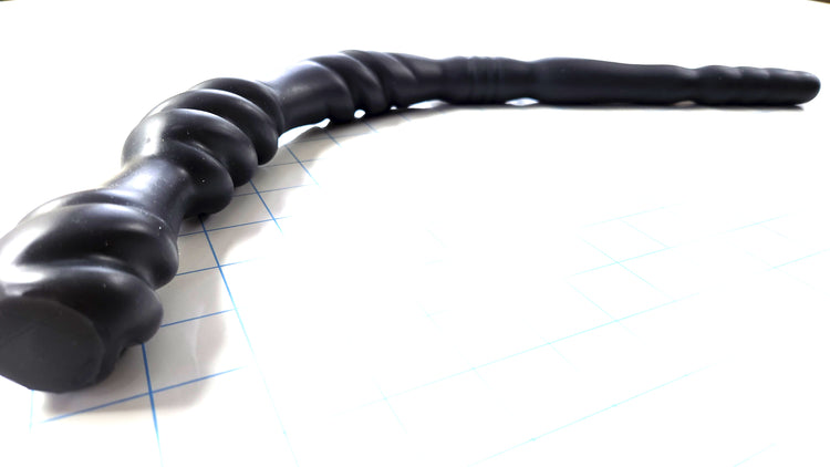 Black Triple Spiral 22-inch silicone nozzle featuring intricate spiraled textures and a graduated design for varied stimulation on a white grid background, showing the flange in focus