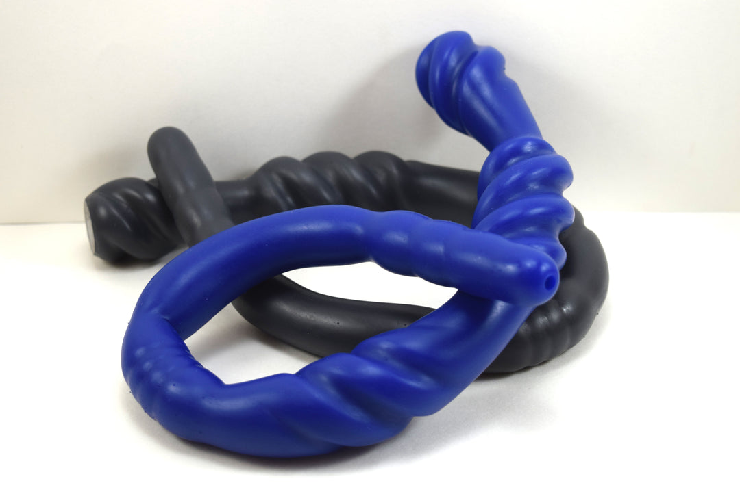 Black and blue Triple Spiral 22-inch silicone nozzle featuring intricate spiraled textures and a graduated design for varied stimulation on a white grid background