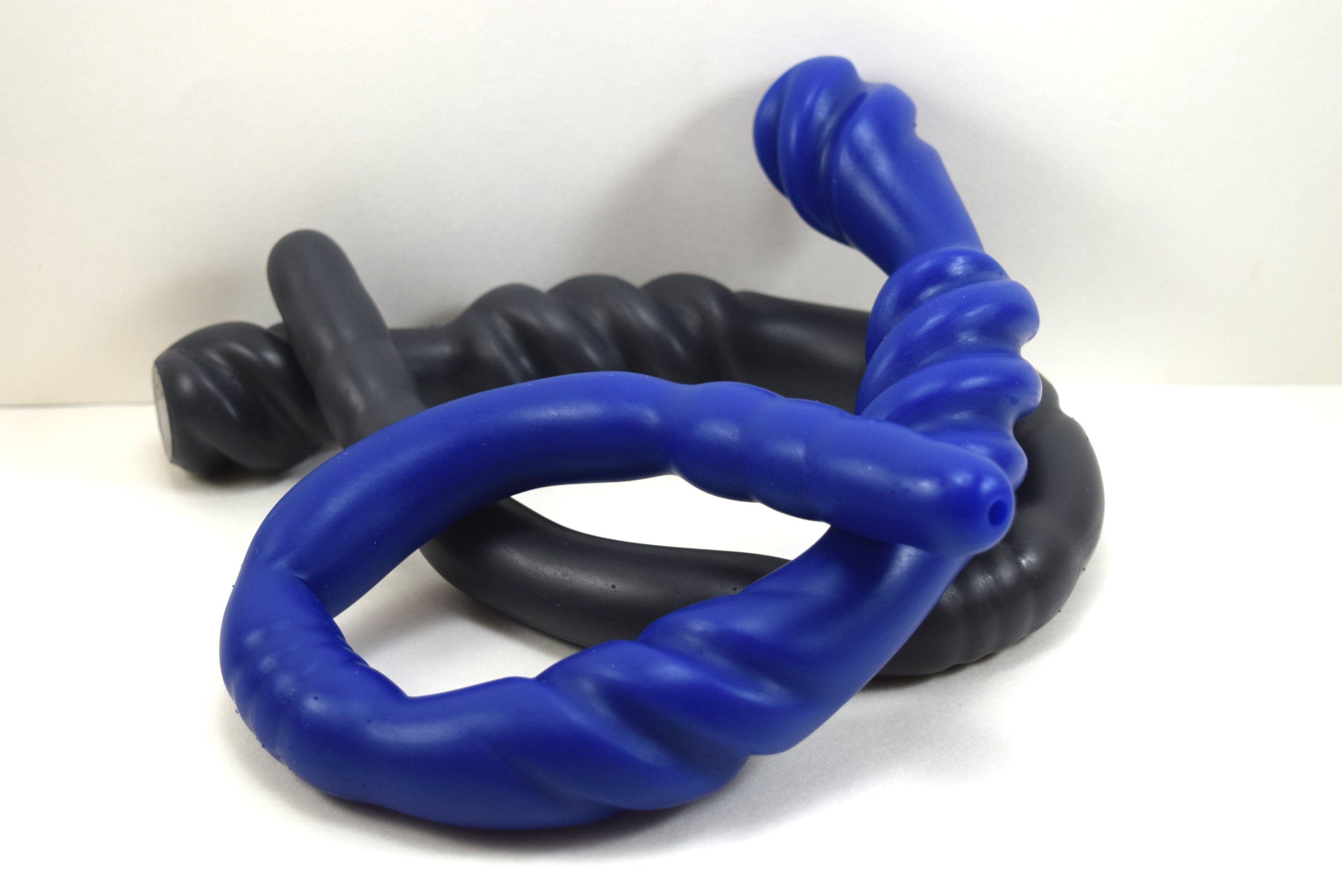 Black and blue Triple Spiral 22-inch silicone nozzle featuring intricate spiraled textures and a graduated design for varied stimulation on a white grid background