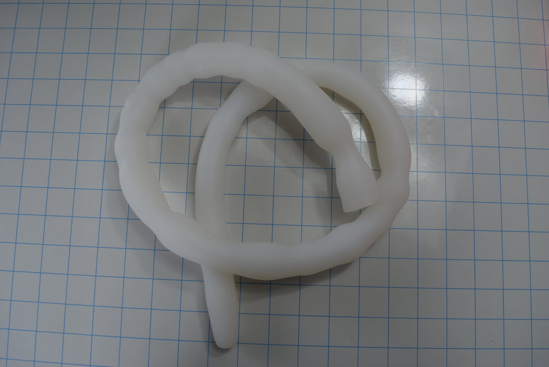 Coiled 39-inch translucent white Shower Shooter XL silicone colon tube on a blue measurement grid demonstrating overall flexibility.