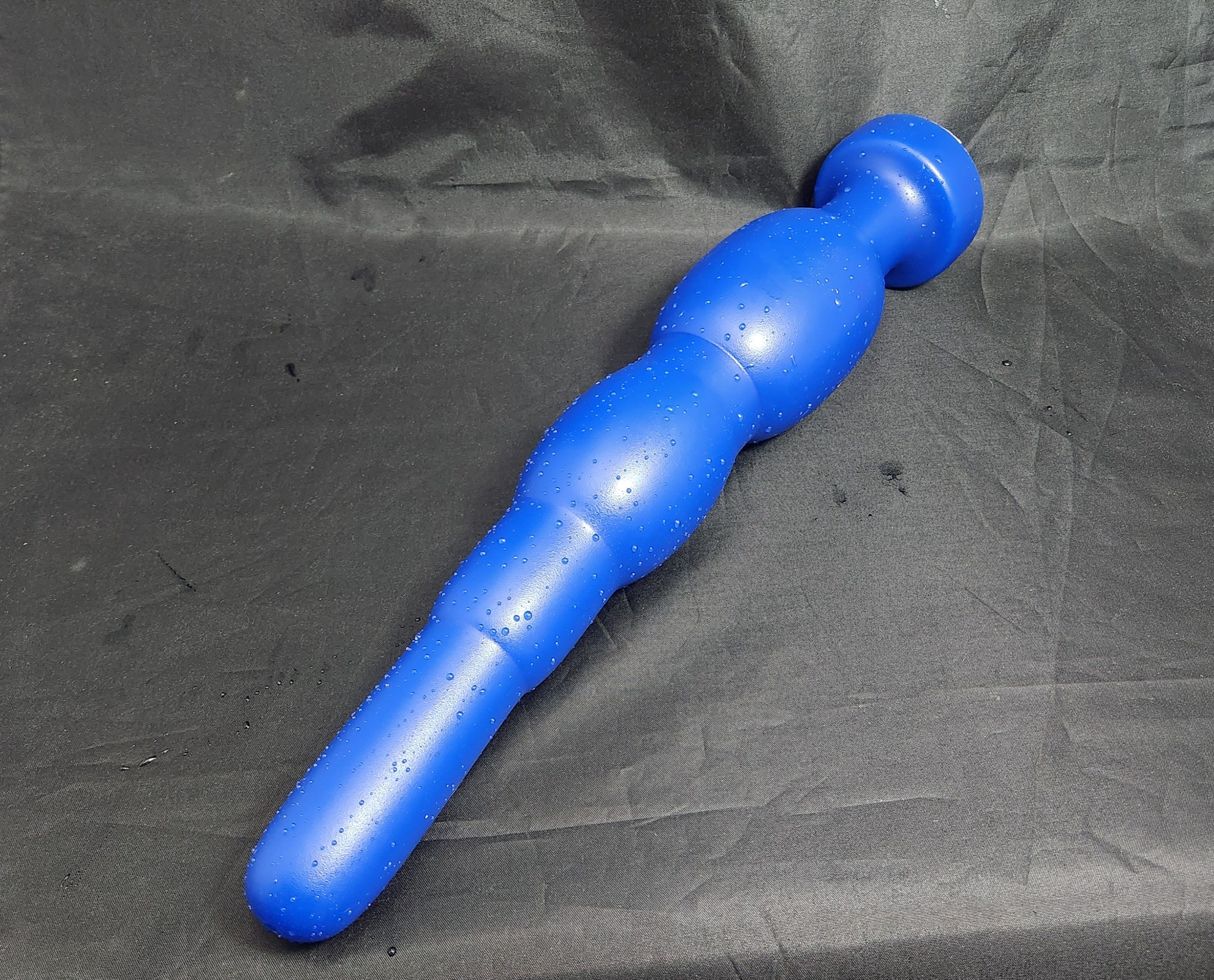 Alternative view of the blue silicone SNC MAX EXT retention nozzle lying diagonally on a grey background, displaying its 14.5-inch insertable length, extended nose tip, and 3-inch retention bulbs.