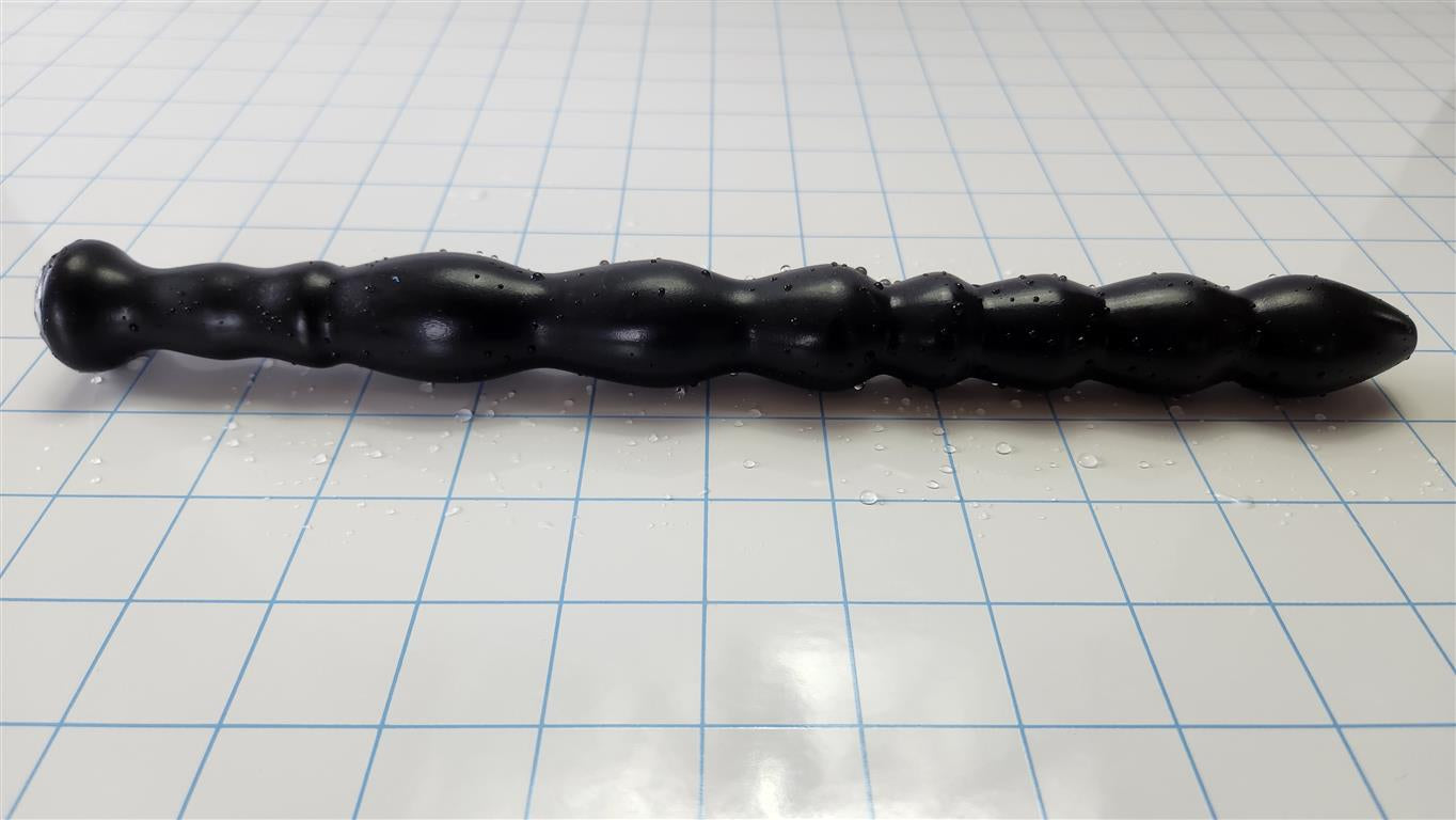 Black Knight 9-sphere undulating silicone enema nozzle lying horizontally across a blue measurement grid.