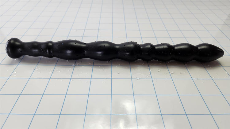 Black Knight 9-sphere undulating silicone enema nozzle lying horizontally across a blue measurement grid.